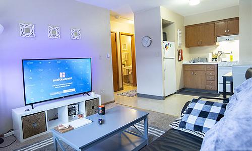Open layout dorm room with tv sitting area and kitchen in view